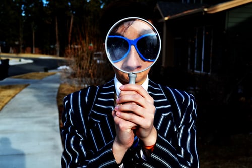 Man holding a magnifying glass in front of his face to demonstrating how to search for hashtags on TikTok. 