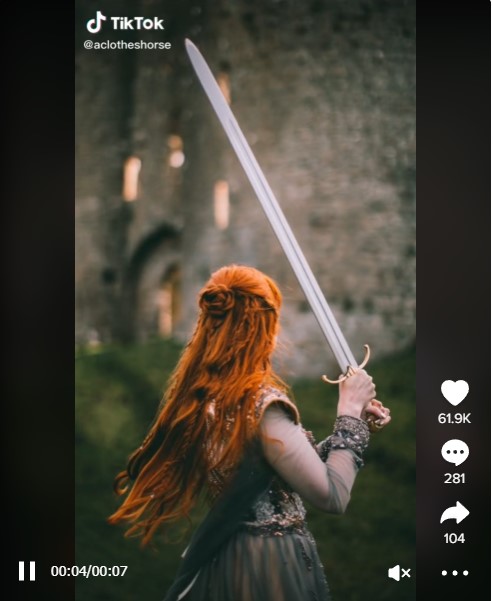 Red-haired woman wearing a medieval dress and wielding a sword for a viral TikTok video.