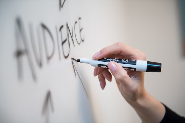 Personne écrivant le mot &quot;Audience&quot; et dessinant des flèches sur un tableau blanc.