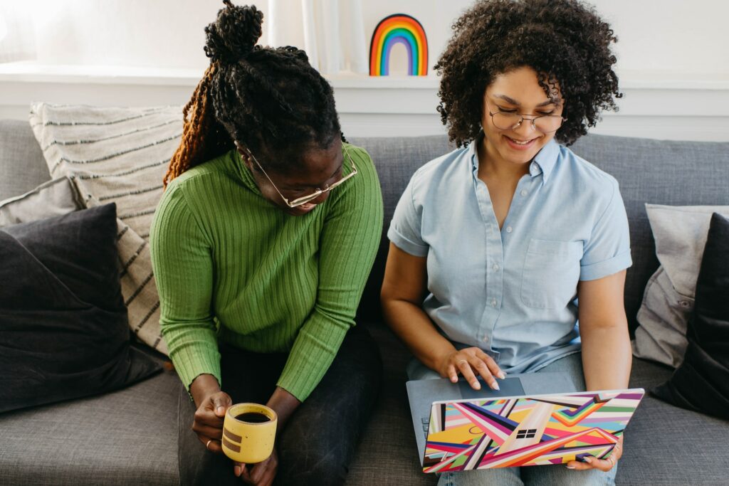 Two women on a couch using a laptop to browse through TikTok videos. 