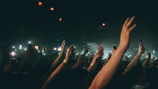 A big audience at a live performance raising their hands. 