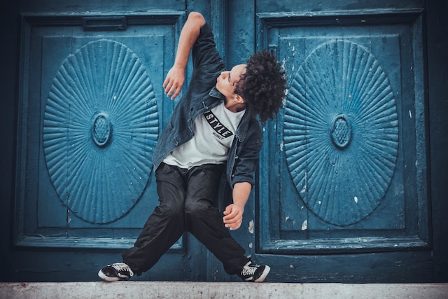 Um homem fazendo movimentos de dança complicados diante de uma porta azul. 