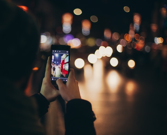A man taking a photo of a busy street at nighttime.