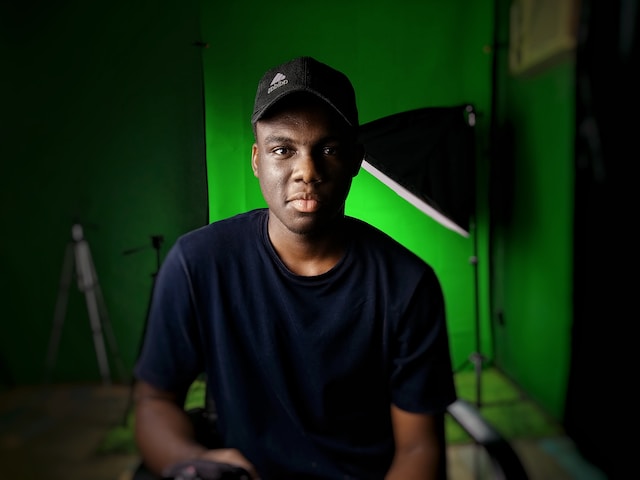  A man sitting in front of a green background. 