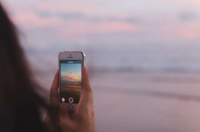 Uma pessoa registrando o pôr do sol com a câmera do celular. 