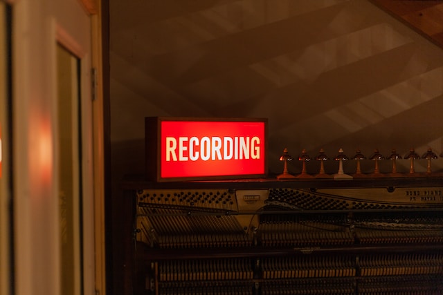 Vermelho e um letreiro de neon branco dizendo "Recording" (Gravação).