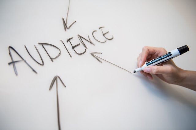 A person writing the word “Audience” and drawing arrows on a whiteboard.