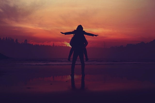 Silhouette eines Mannes, der eine Frau auf seinem Rücken trägt, mit dem Sonnenuntergang im Hintergrund.