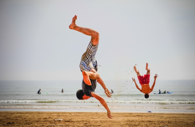 Dois homens dando cambalhotas na praia. 