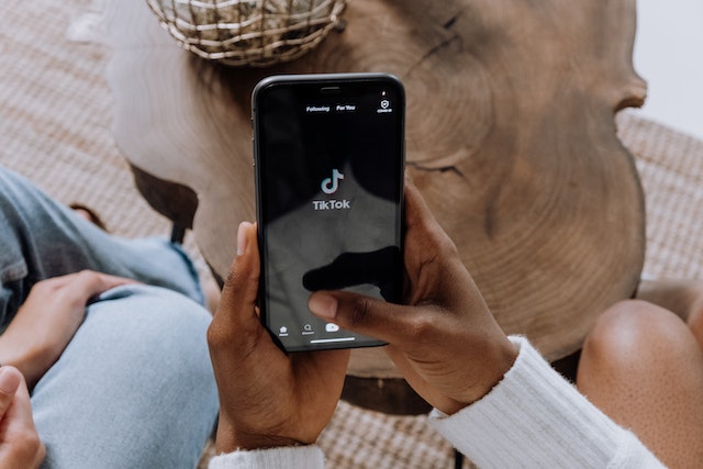 Duas mãos segurando um smartphone com uma tela preta e o logotipo do TikTok, representando o melhor momento para postar no TikTok.