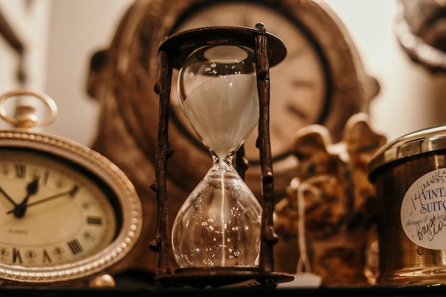 Close-up of hourglass with white sand next to various analog clocks representing various TikTok audience's time zone.