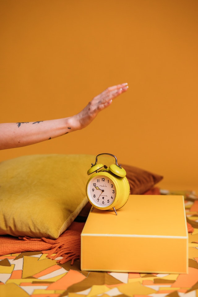 Gele wekker op een gele doos op een mozaïekoppervlak die de beste tijd om te posten op TikTok weergeeft.