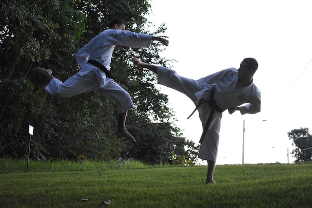 Two men doing karate on a grassy field. 
