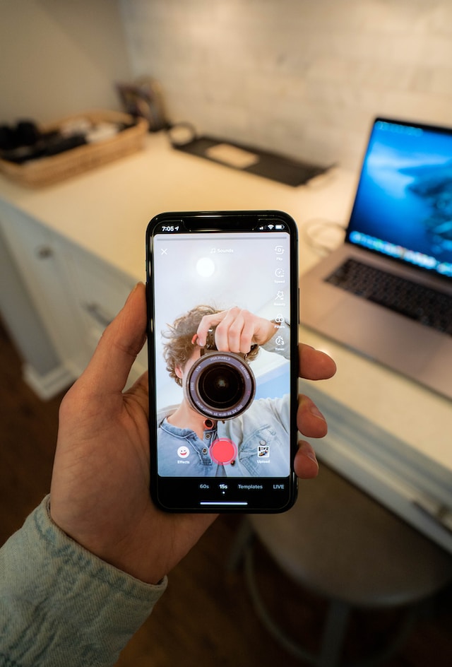A person holding a black smartphone and shooting a video for TikTok.