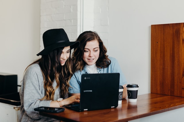 Zwei Frauen schauen sich TikTok-Videos auf einem Laptop an. 