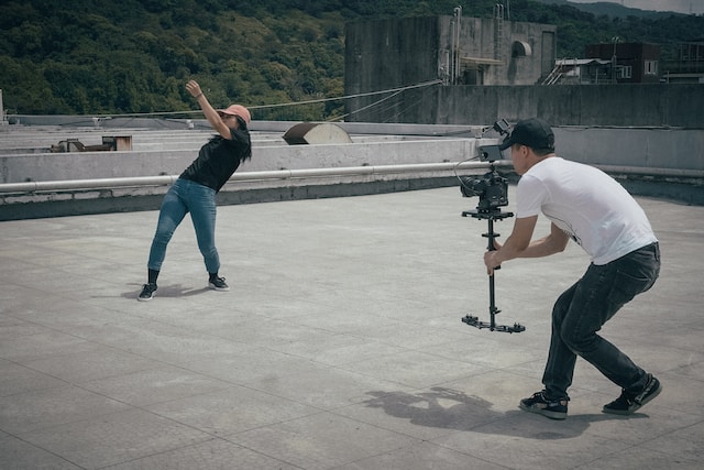 Un bărbat filmează o femeie care dansează pe un acoperiș. 