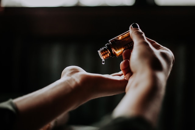 Une personne se verse de l'huile sur la main à partir d'une petite bouteille. 