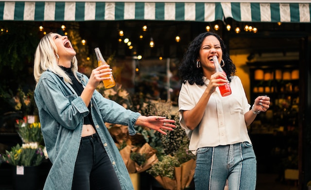 Duas mulheres rindo e fingindo fazer uma apresentação de dueto. 