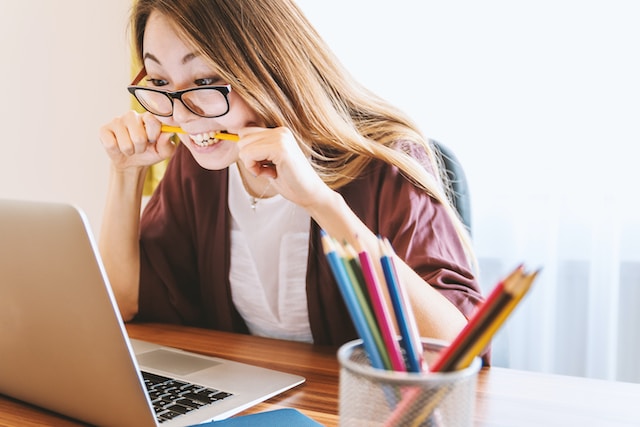 Een vrouw kijkt naar haar laptopscherm terwijl ze op een potlood bijt. 