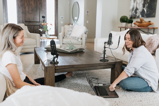 Two women sitting on the floor in front of microphones for a live stream. 