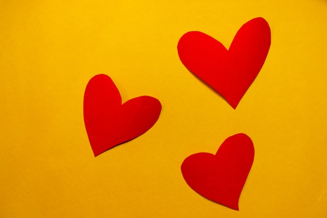 Trois cœurs en papier rouge sur fond jaune. 
