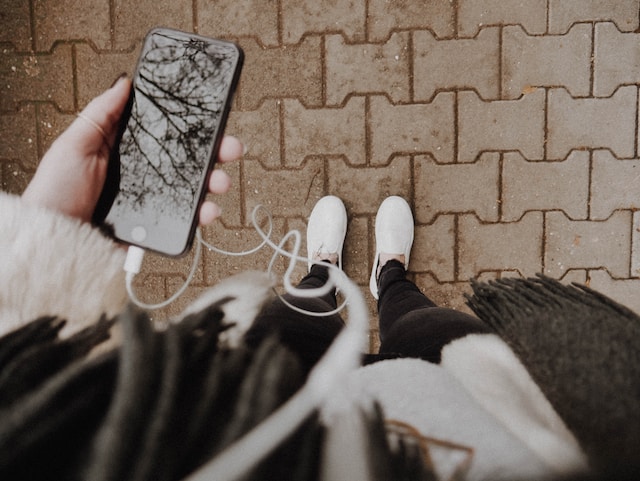 A person holding their phone with earphones attached to it. 