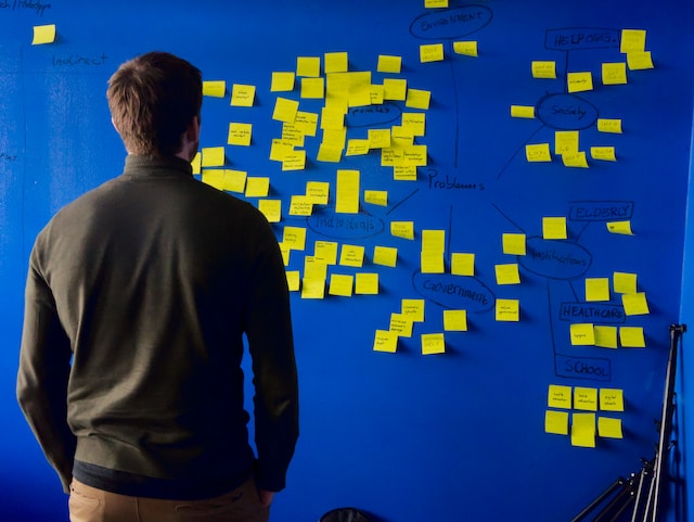 A man standing in front of a board covered with post-its. 