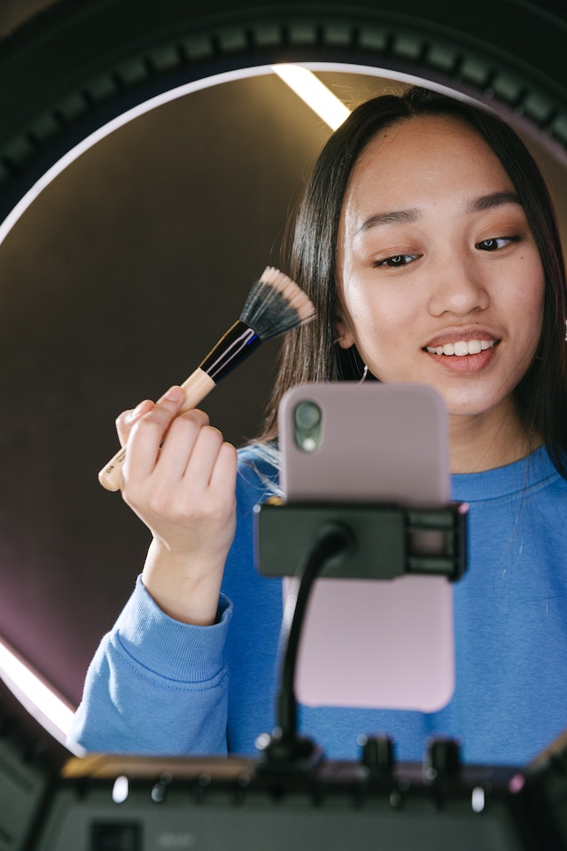 A girl in a blue shirt recording a makeup tutorial video for TikTok. 