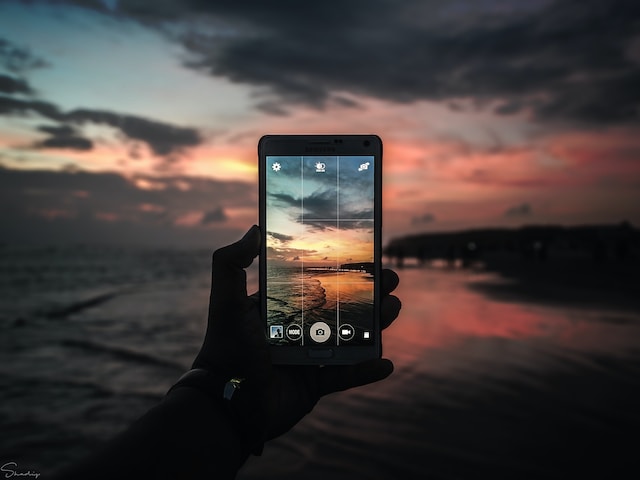 A phone screen displaying a camera grid with the beach at sunset in the background. 