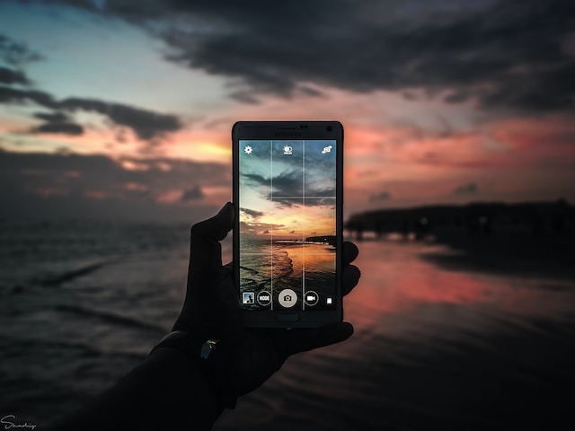 La pantalla de un teléfono muestra la cuadrícula de una cámara con la playa al atardecer de fondo. 