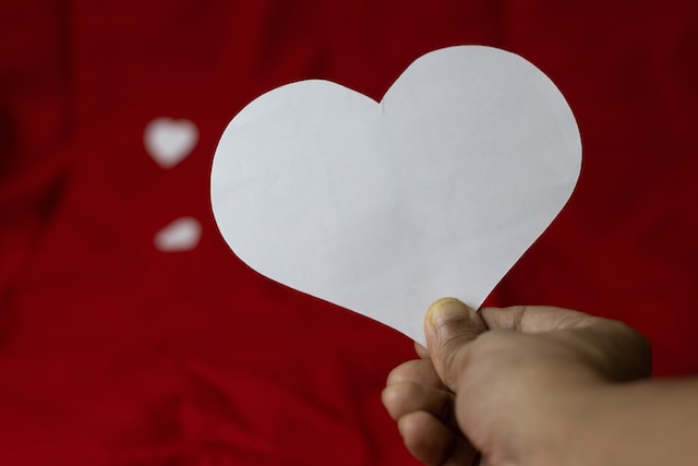 A person holding a white, heart-shaped paper cutout. 
