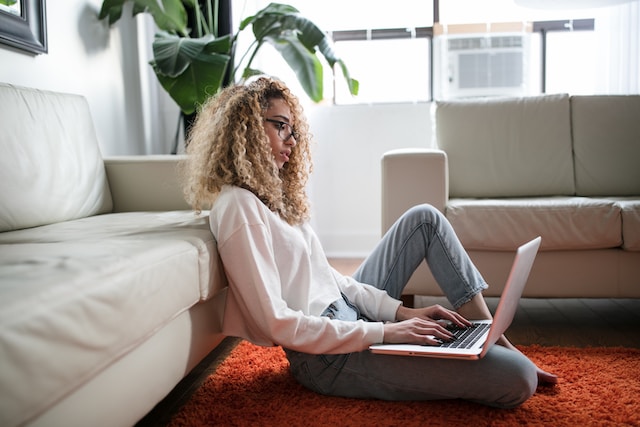 Een vrouw zit op de grond commentaar te typen op haar laptop. 