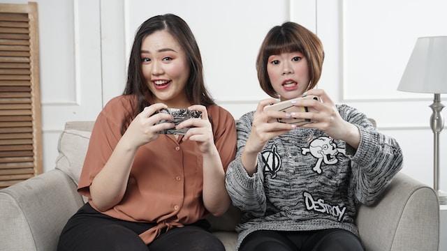Dos mujeres usando sus teléfonos y compartiendo sofá. 