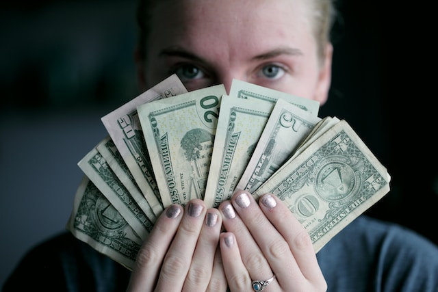 Uma pessoa segurando notas de dólar na frente do rosto. 