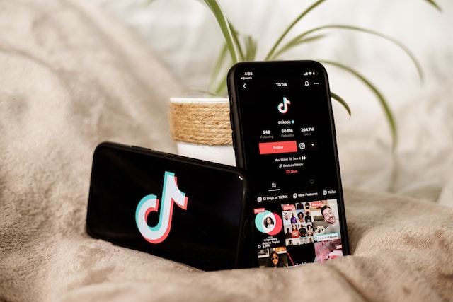 Dois telefones celulares apoiados em um vaso sobre uma cama exibindo a interface do TikTok.