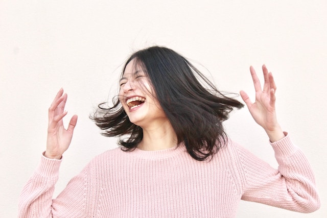 A woman in a pink sweater flicking her hair and laughs. 