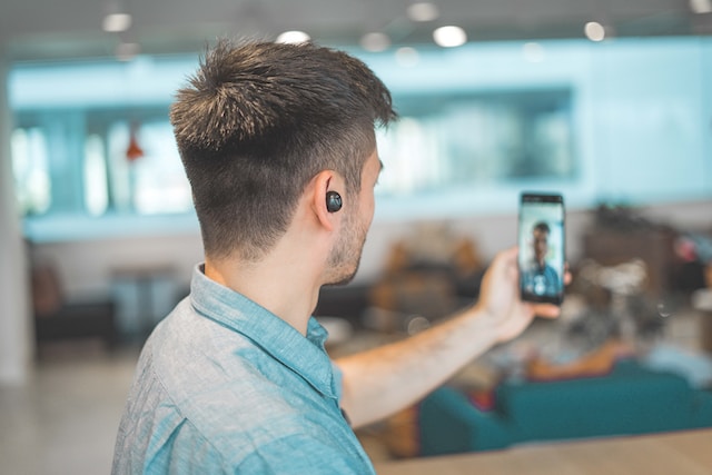 Un uomo in camicia grigia che si fotografa con lo smartphone.