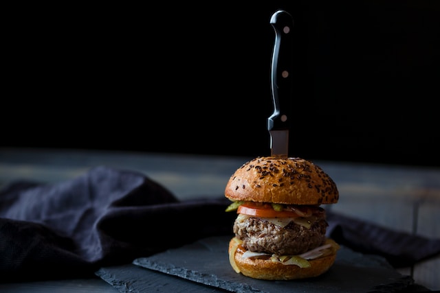 A burger sandwich with a knife sticking out on top. 