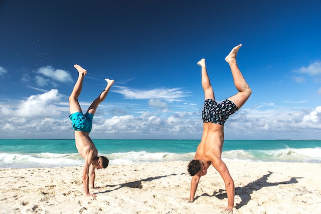 Dois homens fazendo parada de mão na praia. 