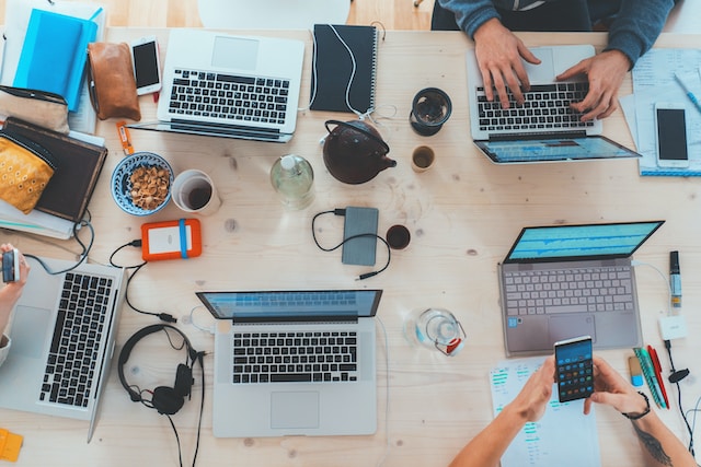 Eine Gruppe von Menschen sitzt um einen Tisch herum und arbeitet an ihren Laptops. 