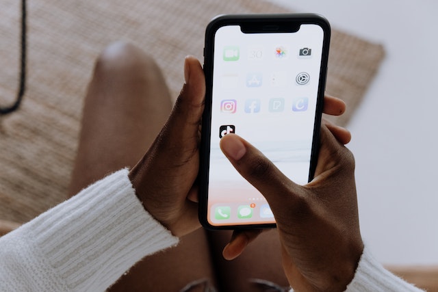 A person holding a smartphone and clicking on the TikTok app. 