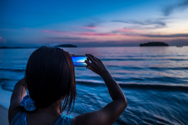 Een dame die een foto van een oceaan maakt met haar smartphone. 