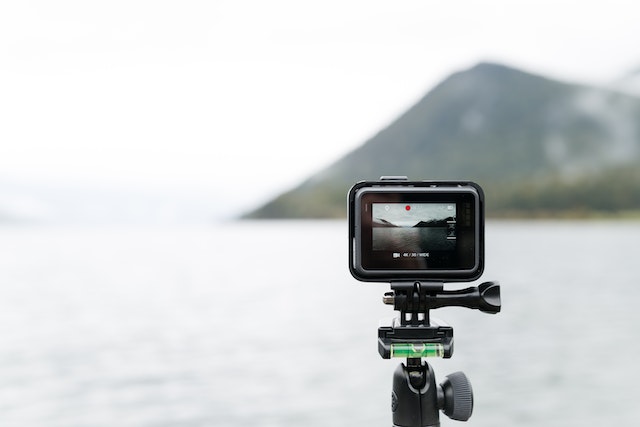 Black action camera recording a view of a lake and a mountain.