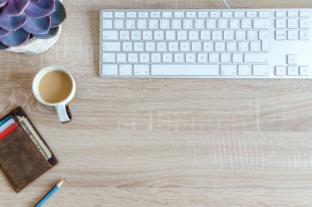 Taza de café cerca de una cartera marrón y un teclado blanco.