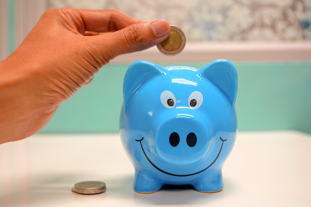 Person putting coins into a blue piggy bank.