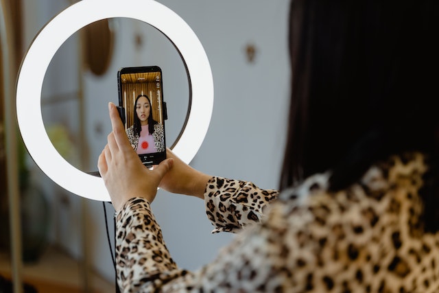 Uma garota gravando um vídeo do TikTok usando um smartphone e um anel luminoso.