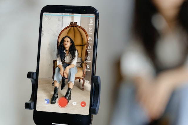 A close-up shot of a smartphone recording a video of a woman sitting on a couch. 