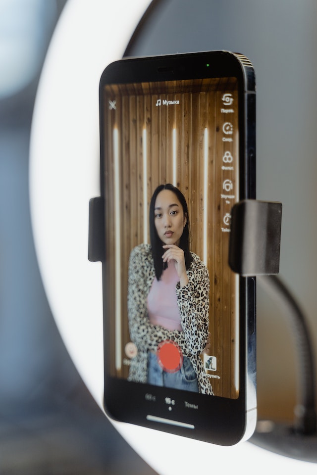 A woman posing at her smartphone camera, recording a video for TikTok. 