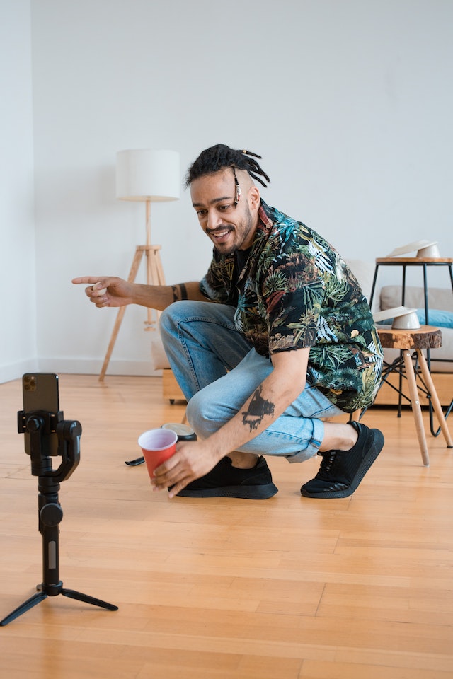 A man in a printed shirt and denim jeans recording a video for TikTok.