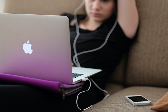 Uma mulher usando fones de ouvido conectados a seu laptop. 